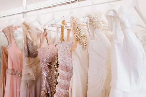 A row of elegant dresses in various shades of pink and white hangs on a clothing rack, perfect for those planning their dream wedding.