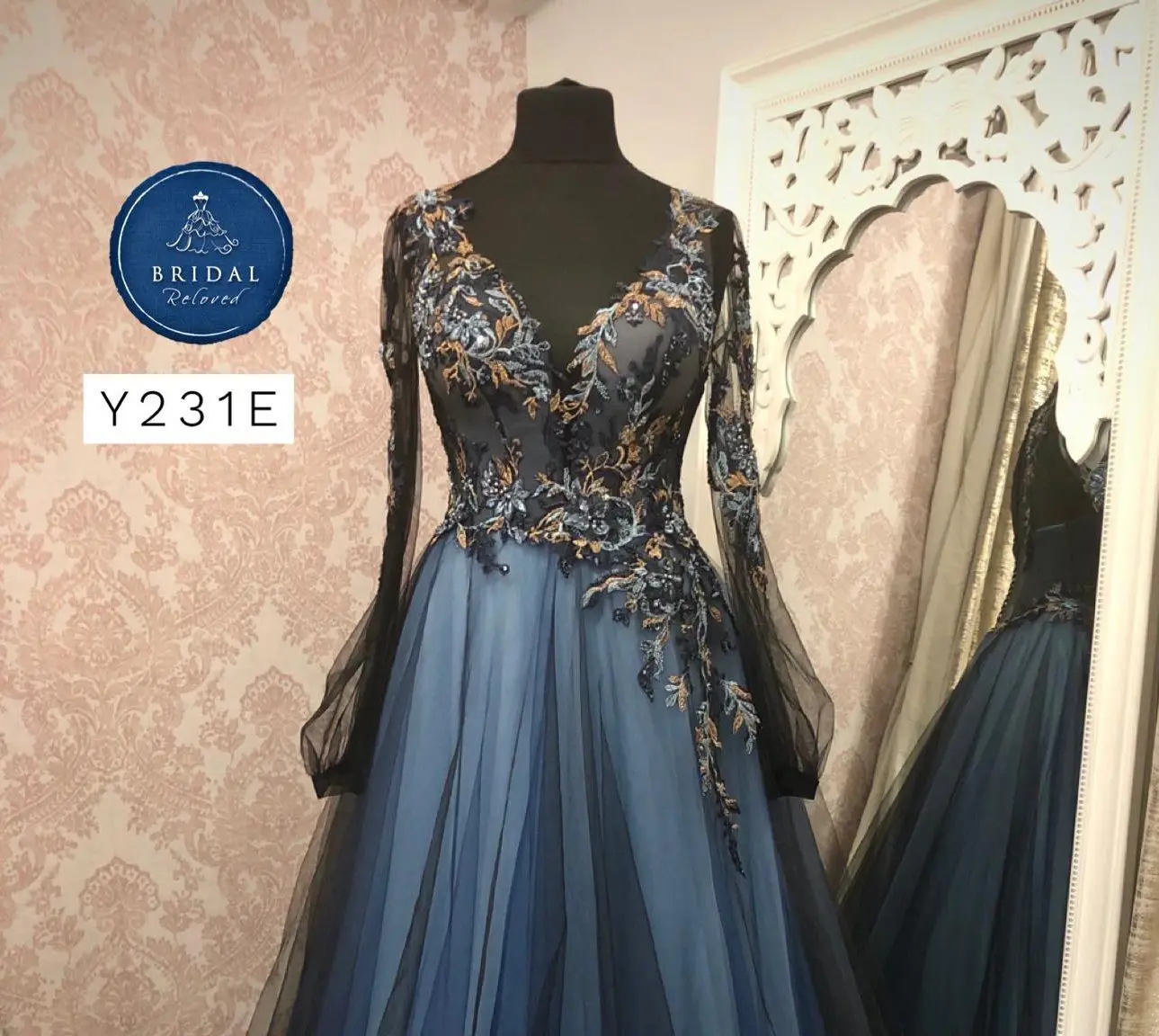 An elegant blue and black dress with floral embroidery is displayed on a mannequin, surrounded by floral wallpaper, perfect for any wedding celebration in the UK.