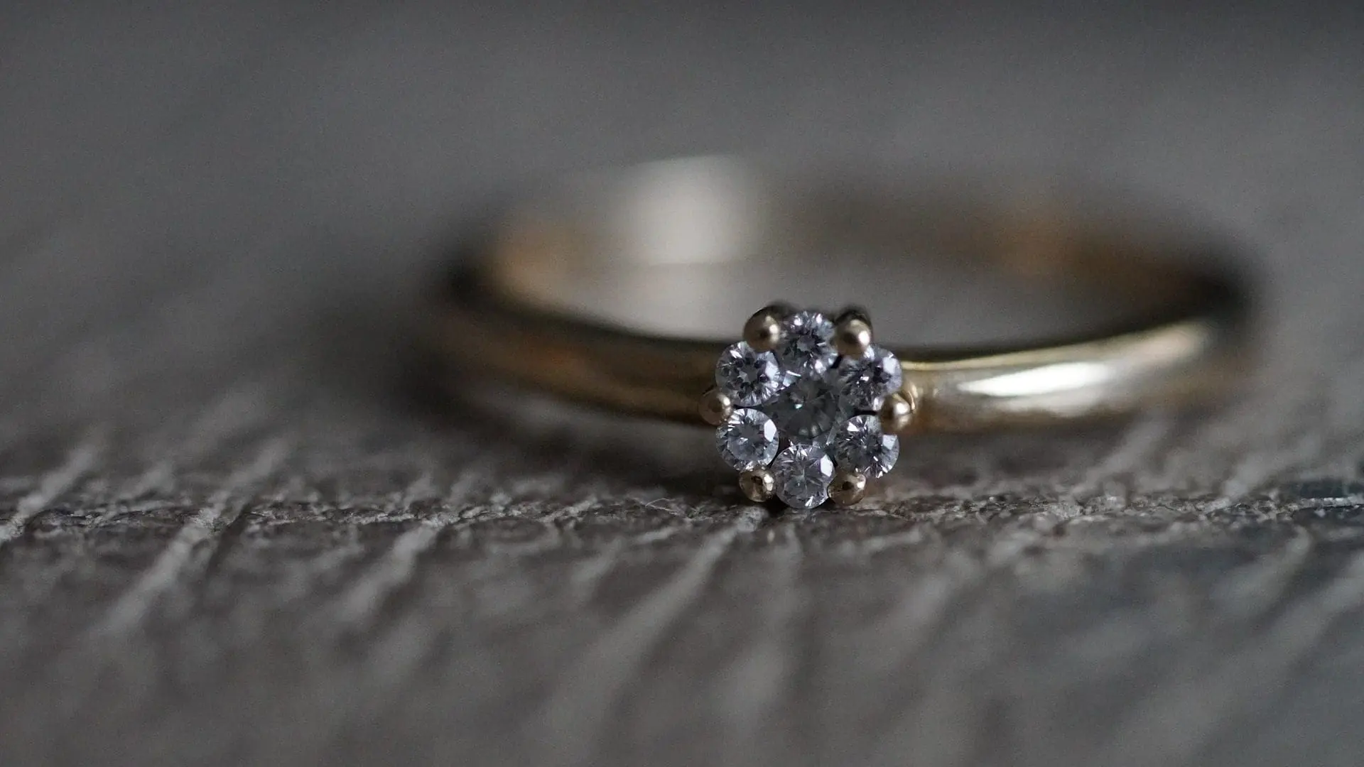 Close-up of a gold wedding ring with a single round diamond on a textured surface.