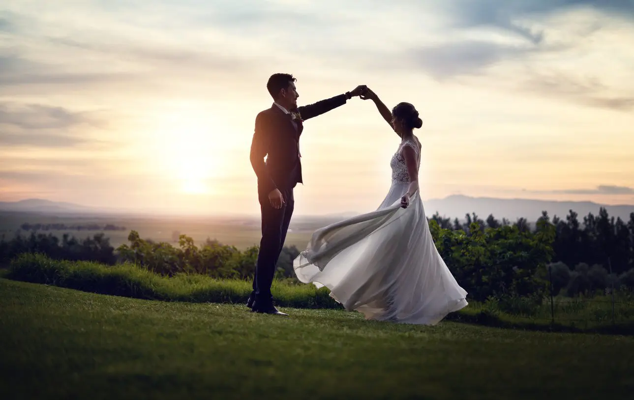 Wedding couple dancing on the top of a hill in the evening sunshine in their wedding outfits.