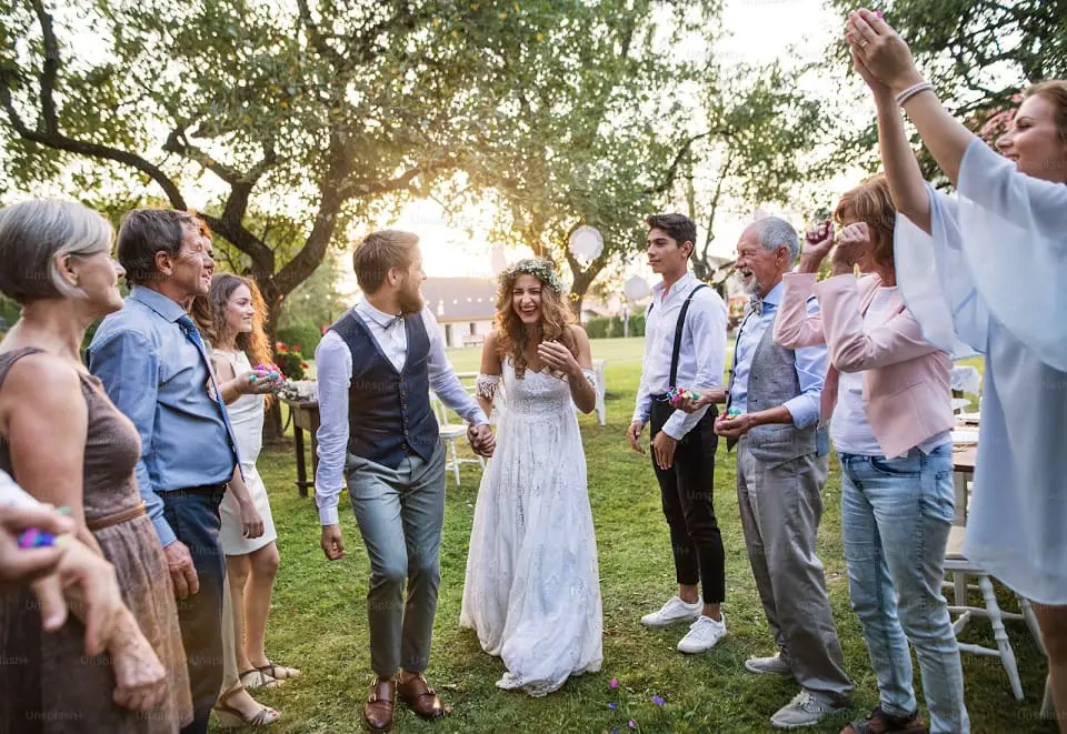 Newlywed couple walking through a line of guests throwing confetti at a sunny outdoor wedding reception.