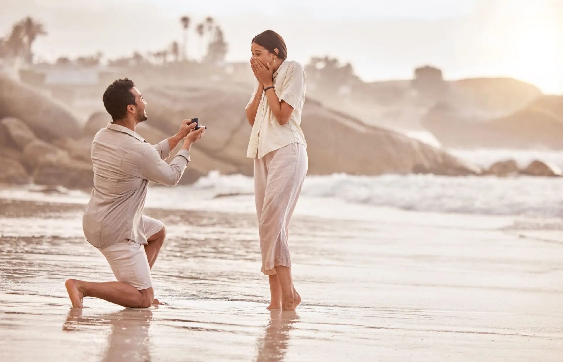 Couple on the beach a surprise proposal with a stunning diamond engagement ring next to the ocean.