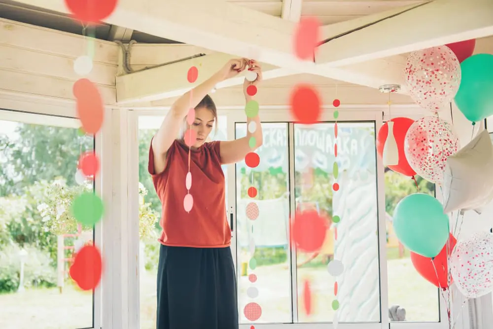 Woman hands orange and green lanterns and streamers from the ceiling ready for a party.