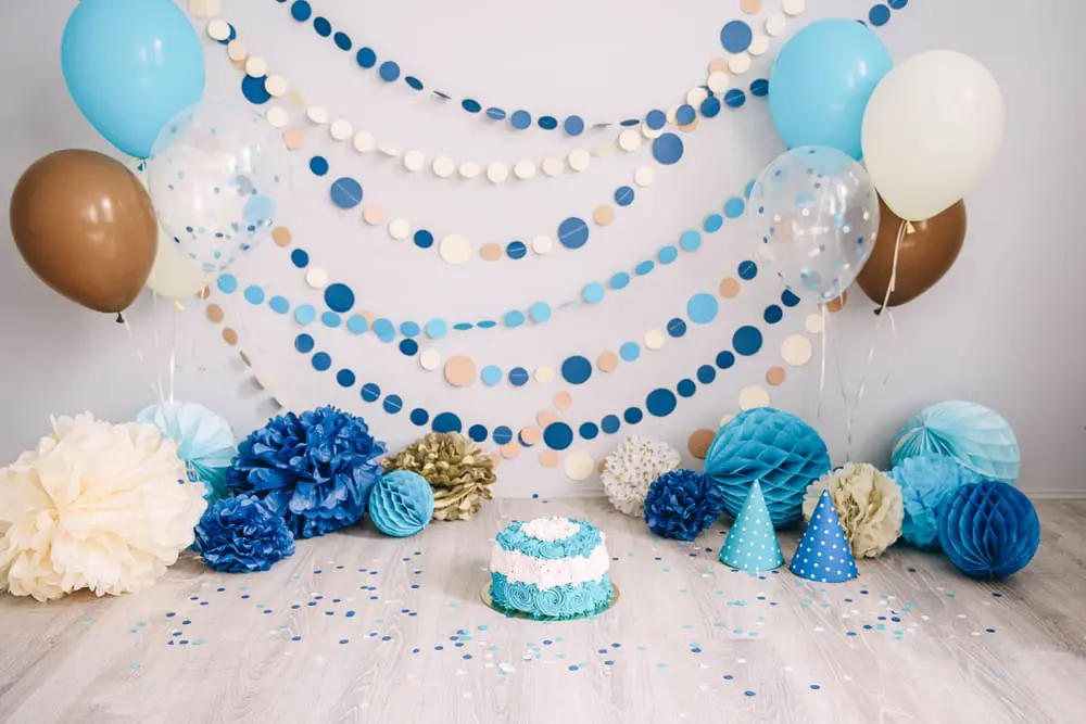 Blue paper garlands with coloured balloons behind a party cake