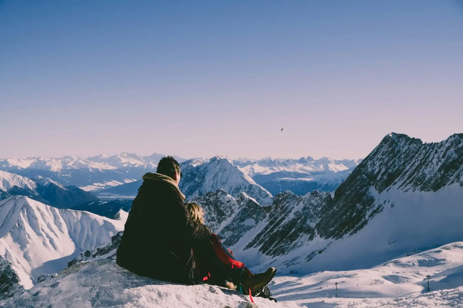 Honeymoon couple on a mountain top looking across snow covered mountains.