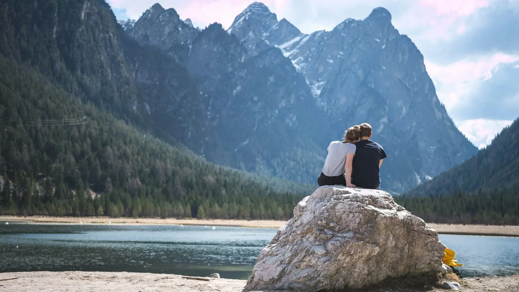 Couple on honeymoon sitting on a rock by a lake looking at the green forest.