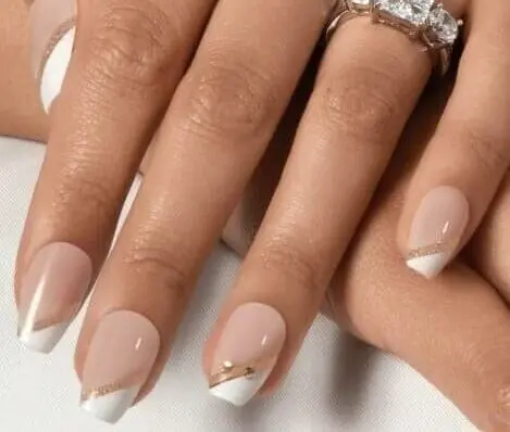 A hand with a white and nude French manicure with gold accents, wearing a ring with three gemstones.