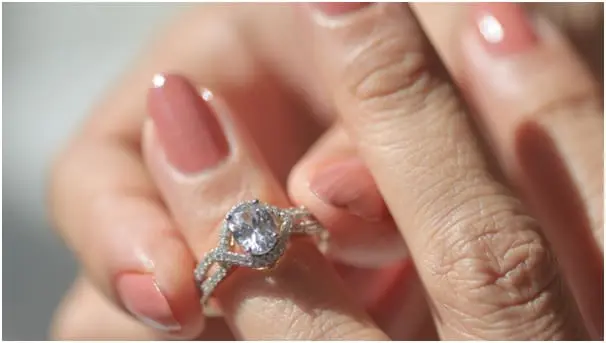 A close-up of a hand wearing a diamond ring with polished nails in sunlight.
