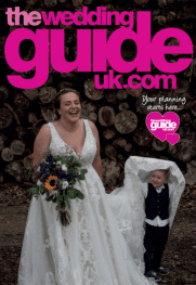 A bride in a white dress holding a bouquet stands beside a smiling child wrapped in a lace fabric. The background shows stacked logs. Pink text reads, "the wedding guide uk.com.