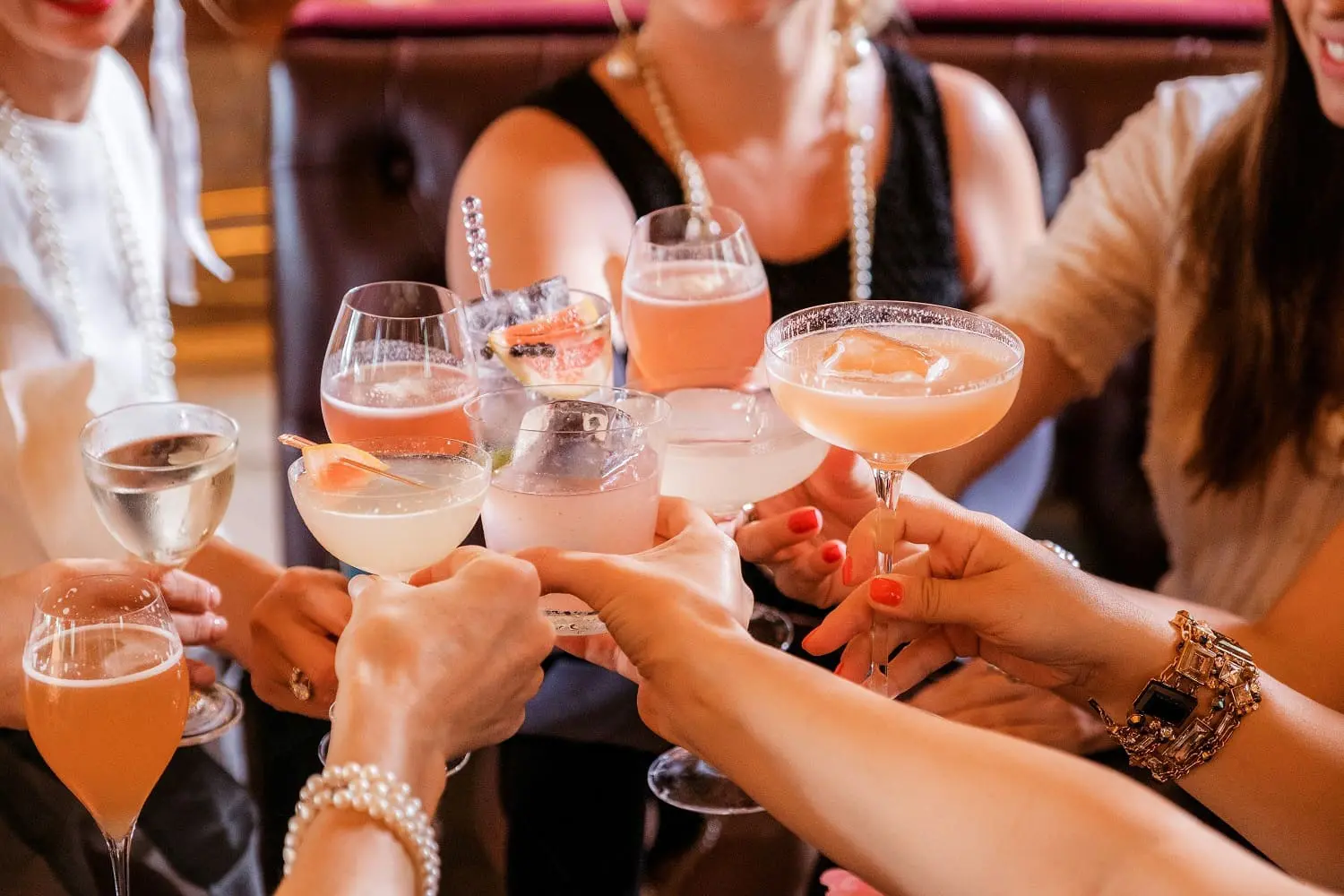 A group of people clinking glasses filled with various cocktails and wine at a table.