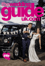 A couple in formal wedding attire stands by a decorated vehicle, smiling and celebrating under a "the wedding guide uk.com" magazine cover.
