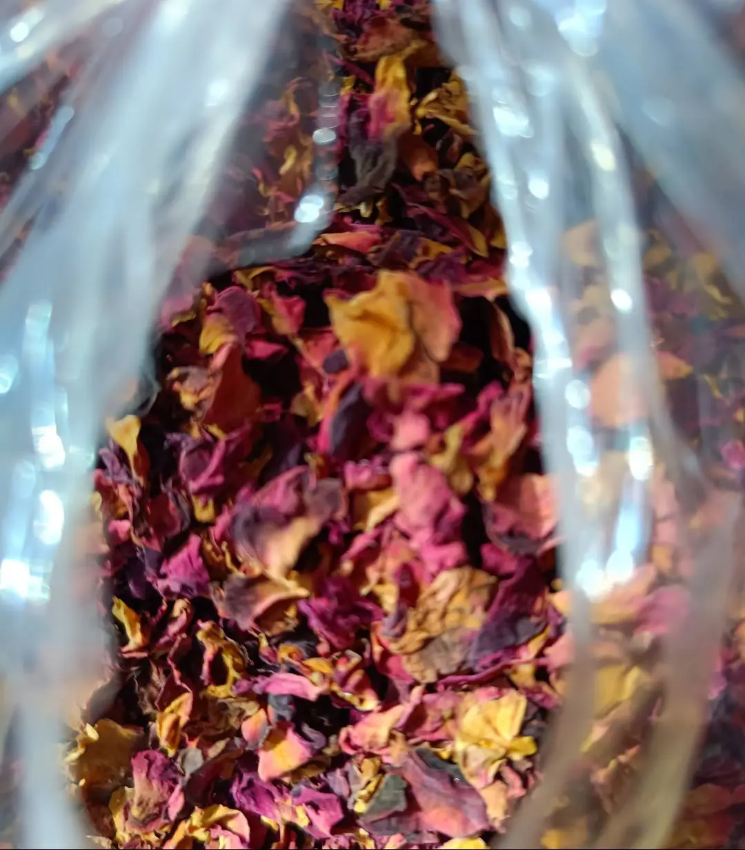 A close-up view of dried rose petals in shades of red, pink, and yellow inside a transparent plastic bag.