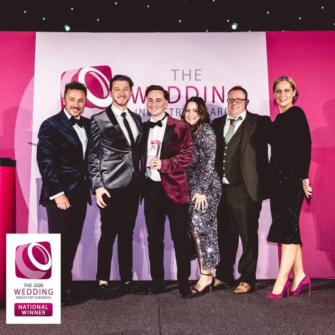 Six people pose on stage at The Wedding Industry Awards event, with one person holding a trophy. A large event logo and "National Winner" sign are visible in the background.