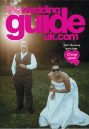 Two people pose outdoors in wedding attire, one in a white dress and one in a waistcoat and tie, featured on the cover of The Wedding Guide UK magazine.