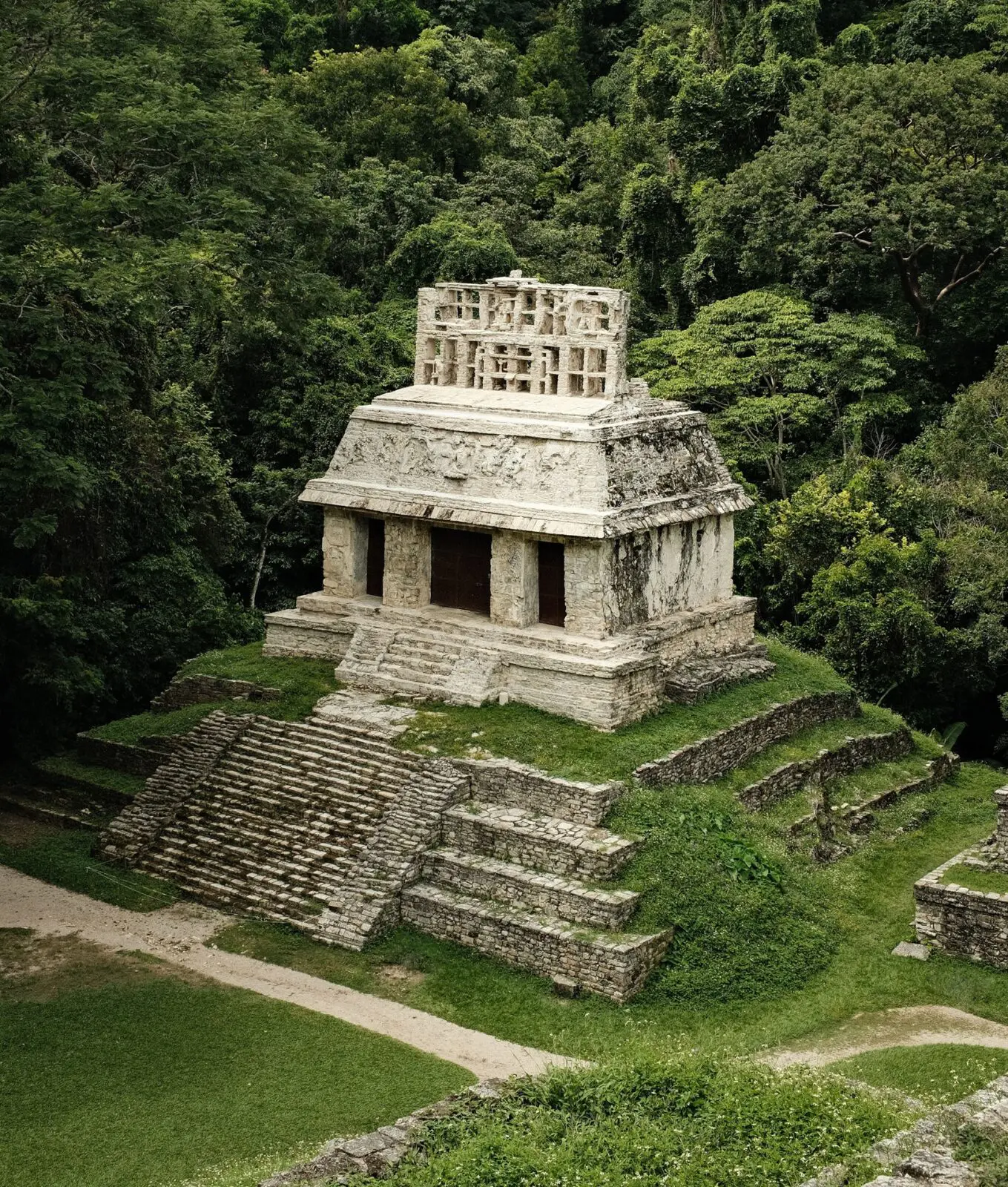 Ancient stone Mayan temple surrounded by dense green jungle, featuring wide steps leading up to a small rectangular structure with intricate carvings on top in Mexico.