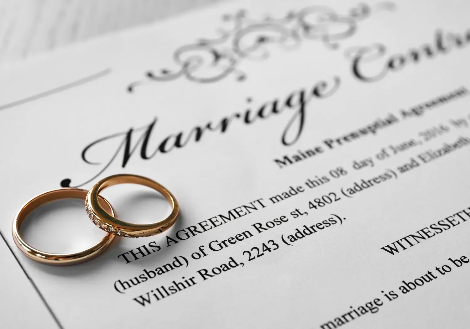Two gold wedding rings rest on top of a marriage contract document, partially visible and printed in black ink.