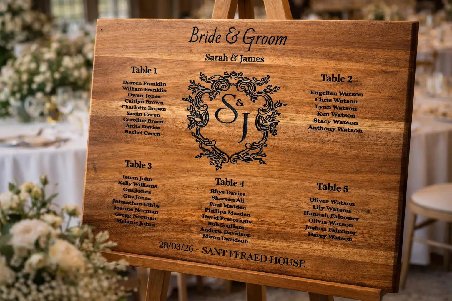 Wedding seating plan on a wooden board listing guests for tables one to five, with the names Sarah and James and the date 28/03/26 at Sant Ffraed House.