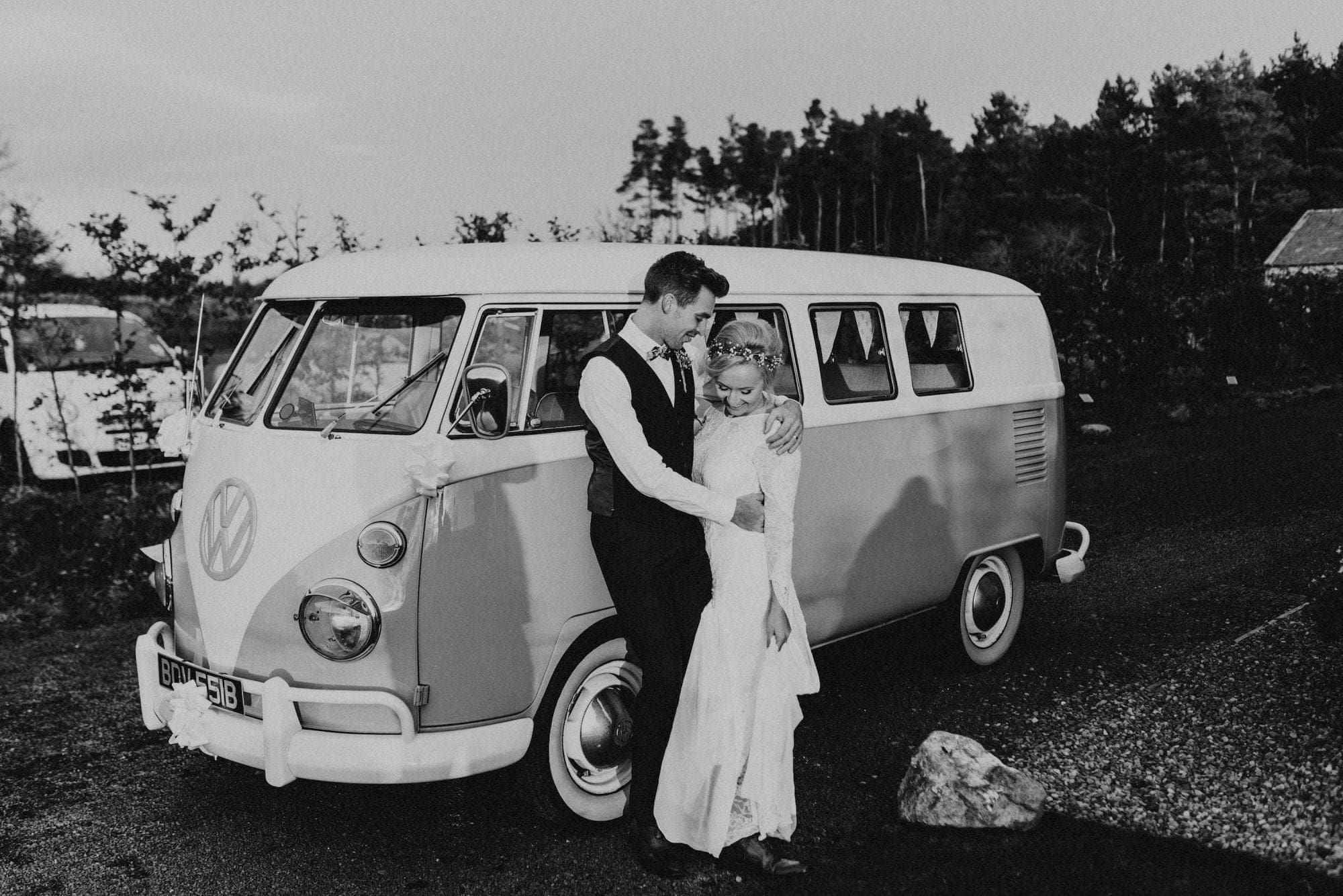 A bride and groom pose next to a VW bus during their wedding.