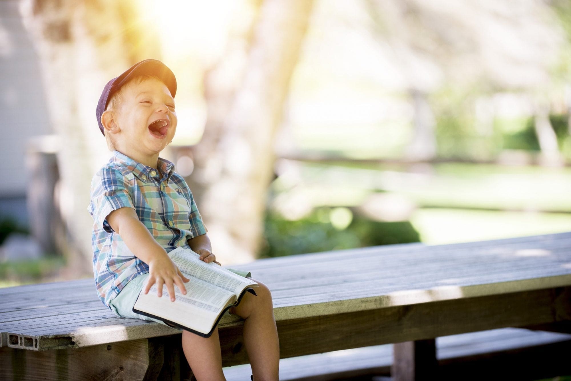A young boy is laughing while sitting on a bench at a wedding.