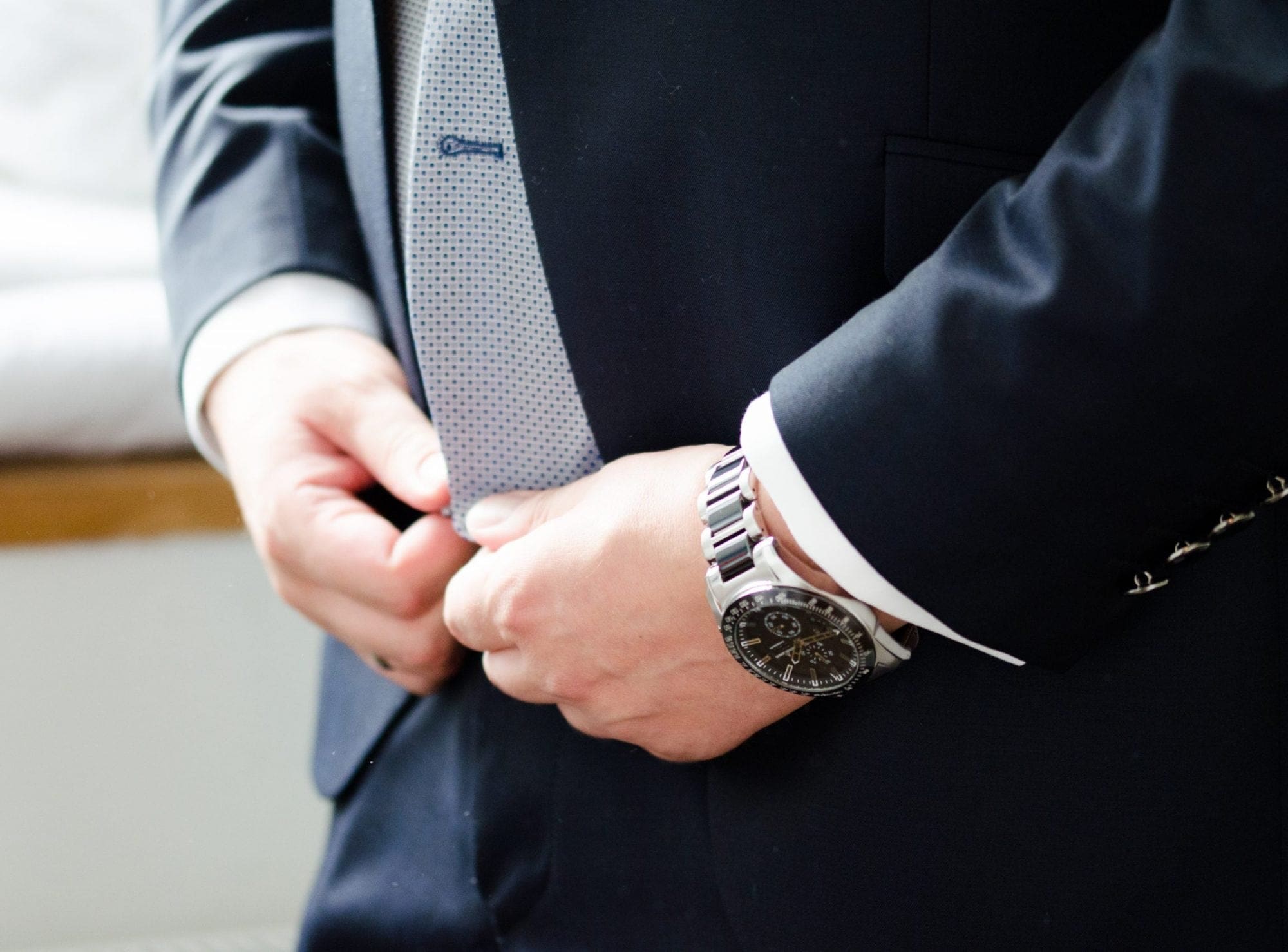 A man in a suit is adjusting his tie, appearing as a suave and professional representative of a wedding business.