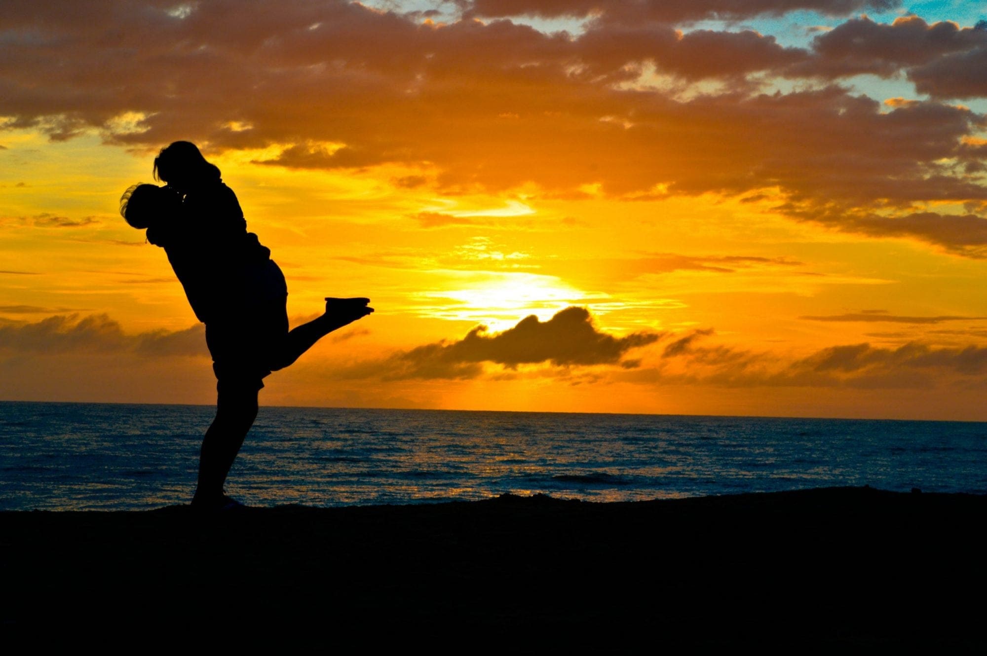 A silhouette of a man on the beach flying a kite.